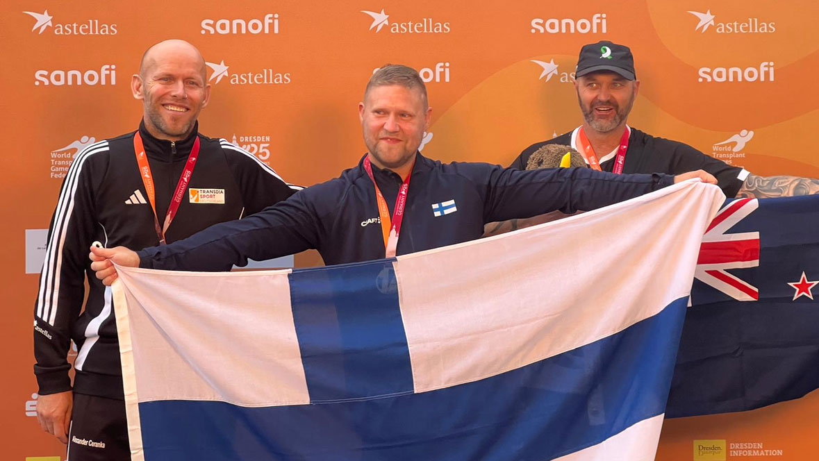 Mikael Kock poseeraamassa kultamitalistina kameralle Suomen lipun kanssa kilpakumppaniensa keskellä. 